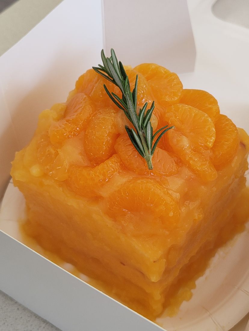Layered mandarin cake topped with rosemary in a white box